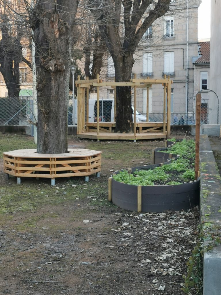 Banc circulaire en bois autour d'un arbre, pergola et bac de culture sur un terrain en cours d'aménagement